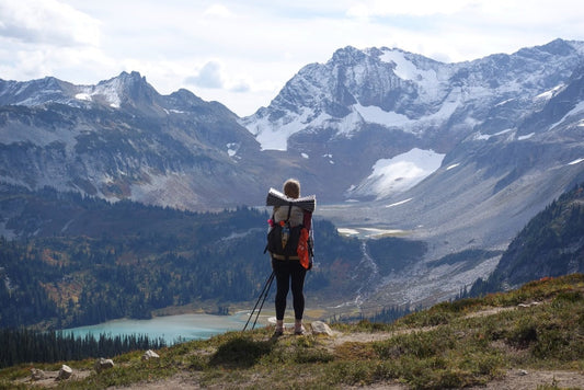 Langstreckenwanderin mit Rucksack auf Thru-Hike in den Bergen – Blick über weite, unberührte Landschaft mit See und Schnee in der Ferne.
