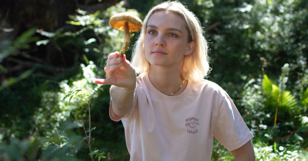 Blonde woman with NIKIN Mushroom shirt looks at a large mushroom in an outstretched hand.