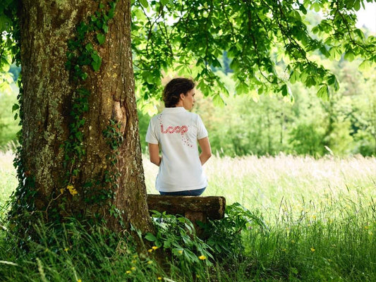 Eine Frau sitzt draußen unter einem Baum und trägt ein weißes Shrit mit einem Loop Logo, das von Pandinavia stammt.