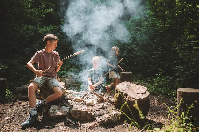 Trois enfants sont en train de faire griller du pain au serpent sur un feu dans la forêt.