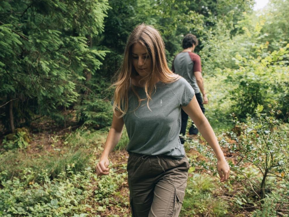 Out and about in the forest, a woman and a man wearing the NIKIN TreeShirt Coffee Carbon.